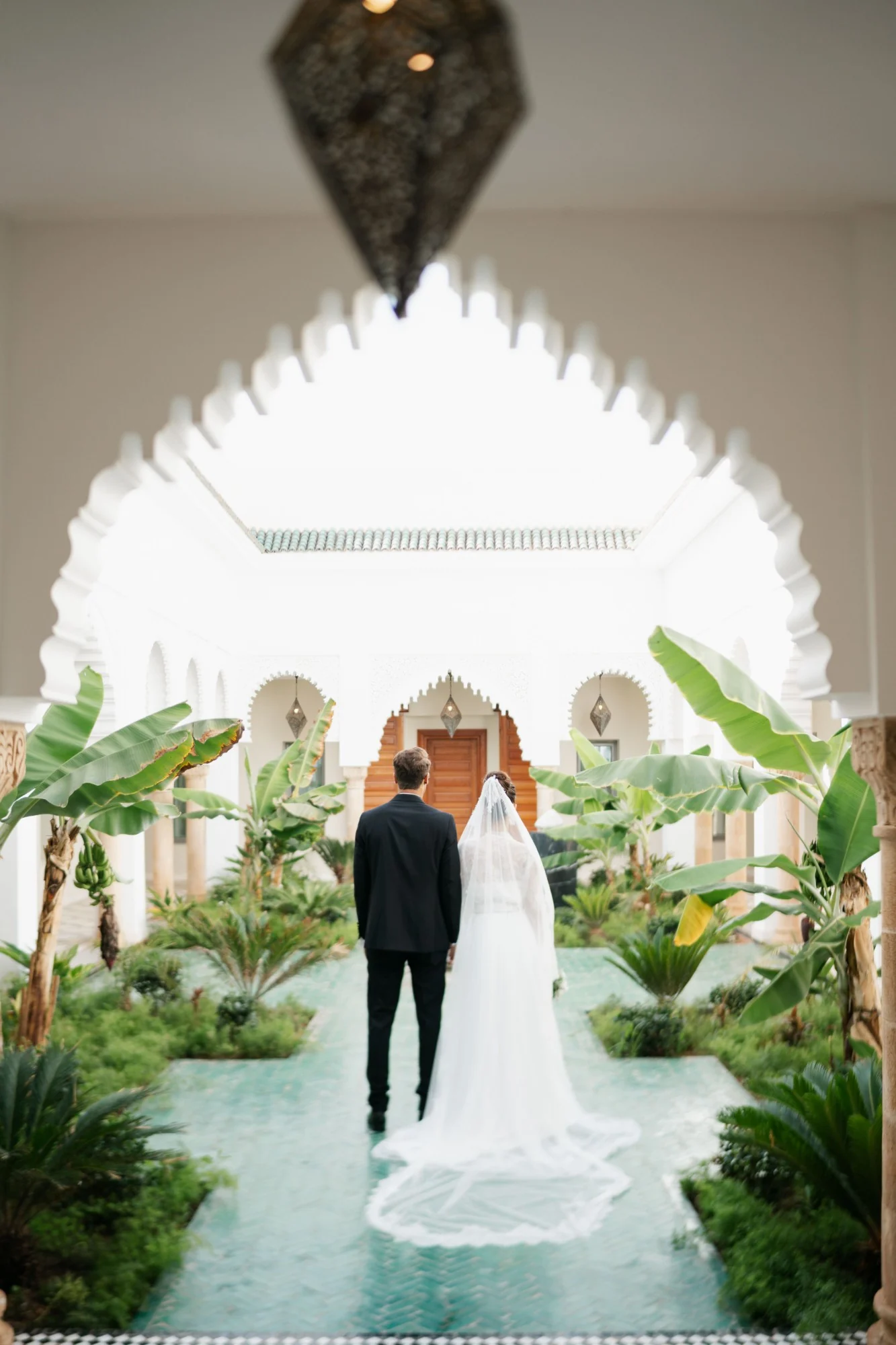 Les mariés de dos sous une arche sculptée, dans le patio fleuri d’un riad